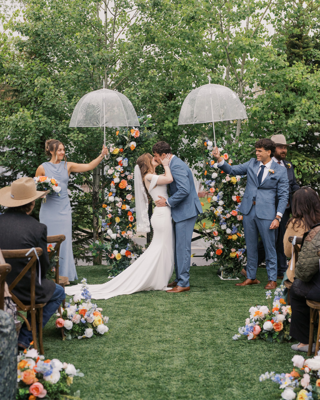 Ceremony first kiss beneath clear umbrellas and florals