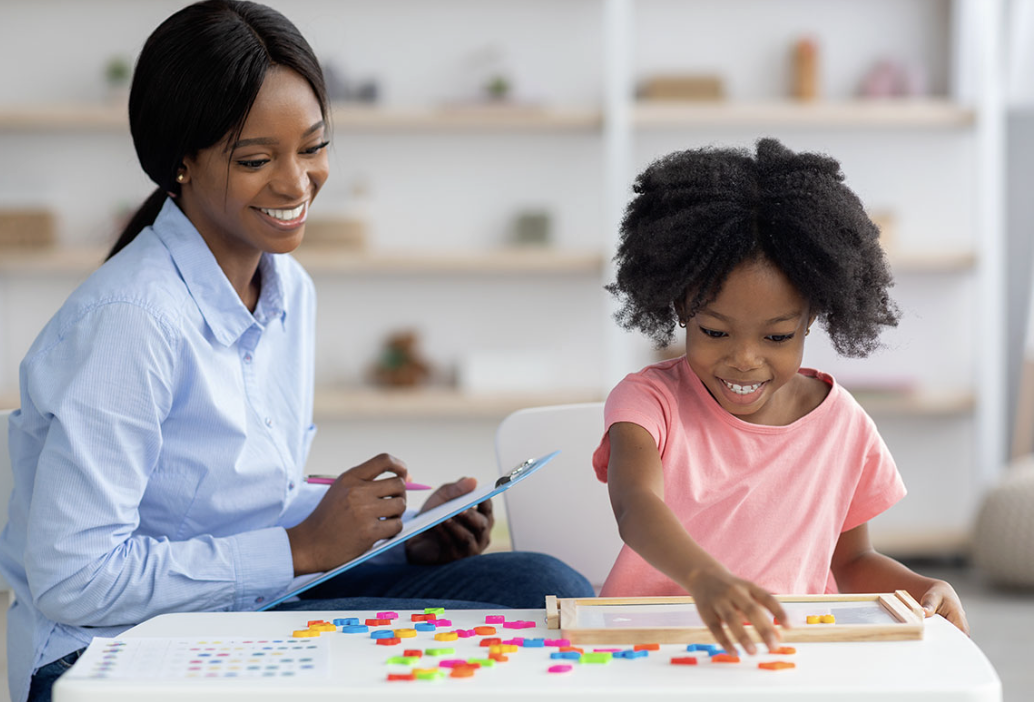 Therapist guiding a smiling child through a colorful table activity